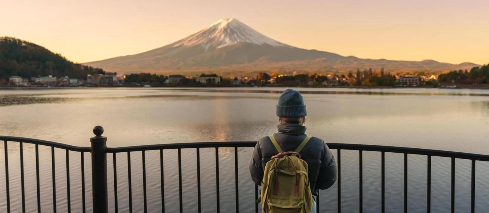 湖越しに富士山を眺めるバックパックの旅行者