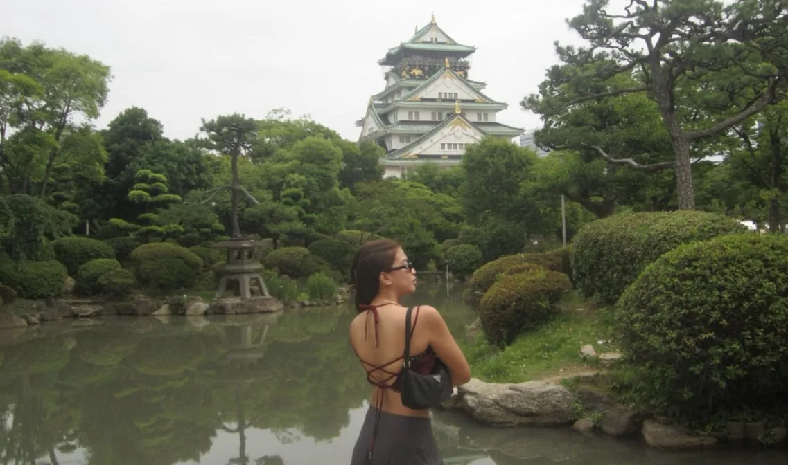 城の天守を望む日本庭園の池のほとりに立つ旅行者